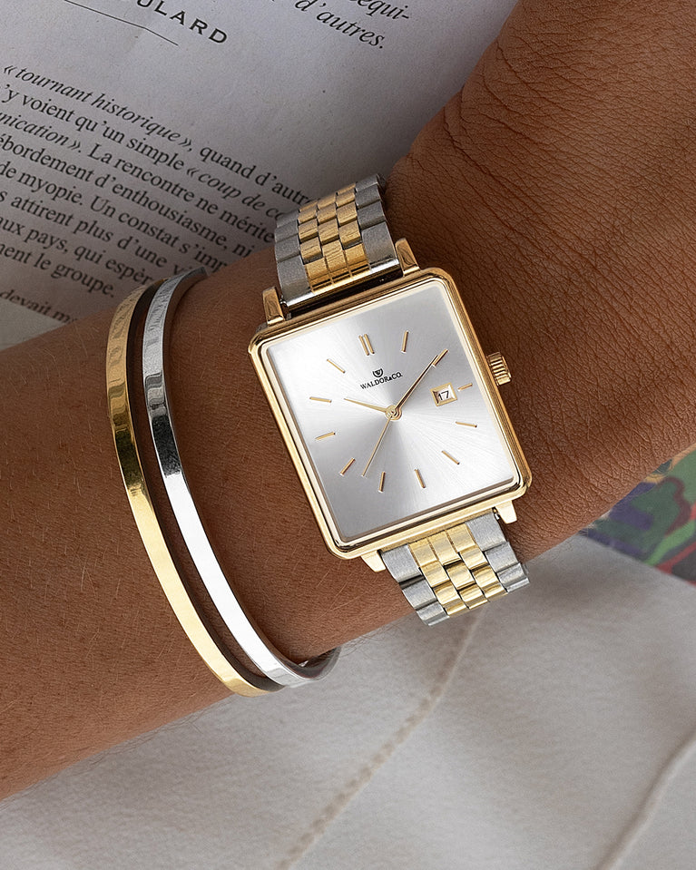 A square womens watch in silver and 14k gold from Waldor & Co. with silver sunray dial and a second hand. Seiko movement. The model is Delight 32 Chelsea 28x32mm.