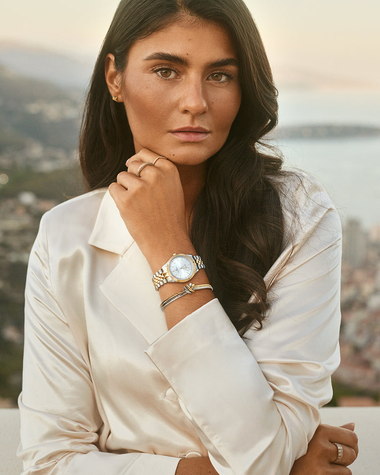 A round womens watch in silver and 22k gold from Waldor & Co. with silver sunray dial and a second hand. Seiko movement. The model is Imperial 32 Positano 32mm.