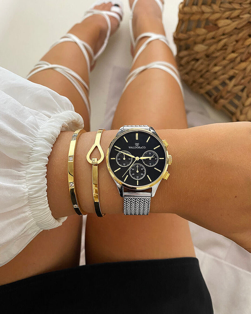 A round womens watch in14k gold-plated 316L stainless steel from Waldor & Co. with black dial  and a second hand. Seiko movement. The model is Epoch 36 Formentera 36mm.